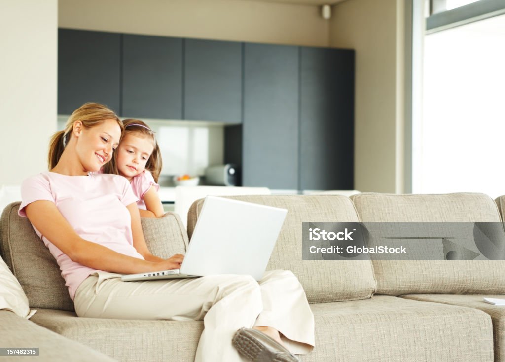 Mother using laptop with daughter standing beside her  Daughter Stock Photo