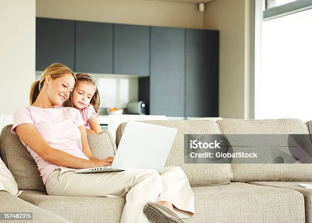 Mother Using Laptop With Daughter Standing Beside Her Stock Photo - Download Image Now