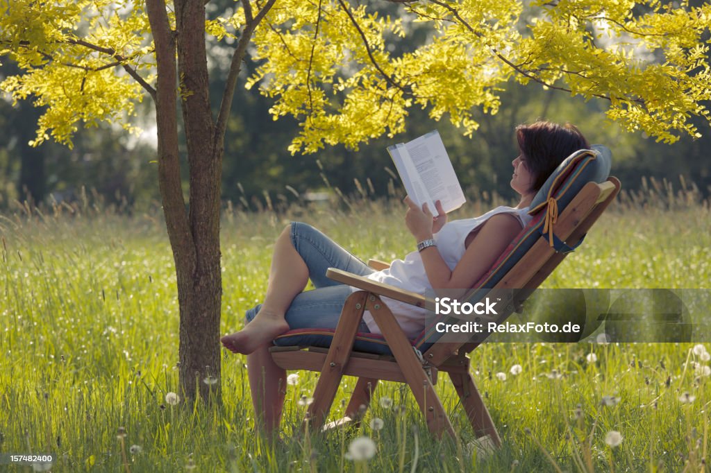 Jeune femme sur la terrasse en bois, chaise de lecture livre sous arbre - Photo de Femmes libre de droits