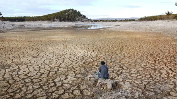 Young man sitting helplessly in a pond drained by drought.