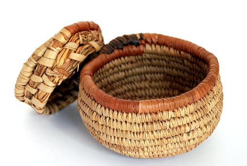 A small, round, handmade African basket on a white background. The basket is open, with the lid leaning against it.