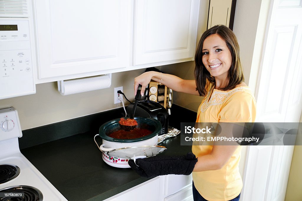 Smiling Young Woman Serving Chili Out of  a Crock Pot Smiling Woman Serving Chili at home in the Kitchen Crock Pot Stock Photo