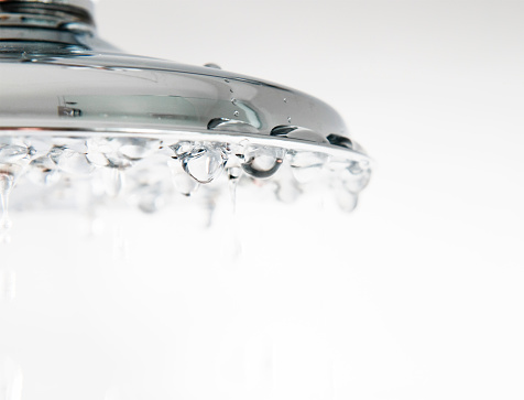 Droplets of water falling from a chrome shower head.  Shallow depth of field, sharp focus on the droplets halfway across the shower head.