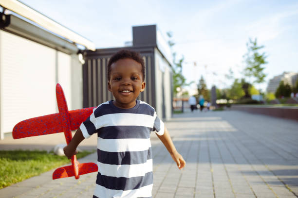 istock A young African American boy is cheerfully looking at the camera, while holding a plane toy 1574846231