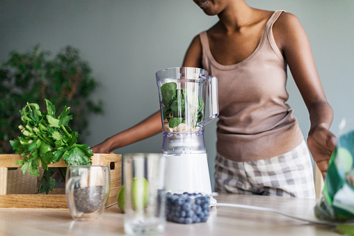Young adult black woman making smoothies for breakfast in the morning