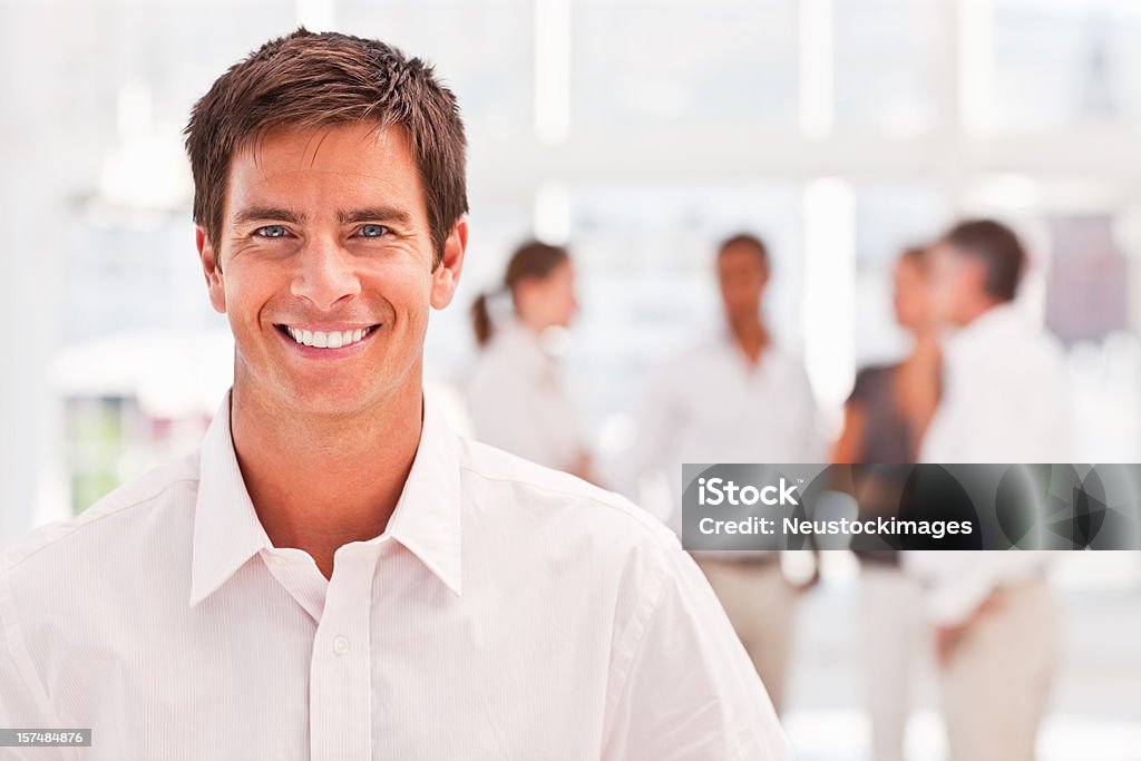 Uomo d'affari sorridente con i colleghi in background - Foto stock royalty-free di 20-24 anni