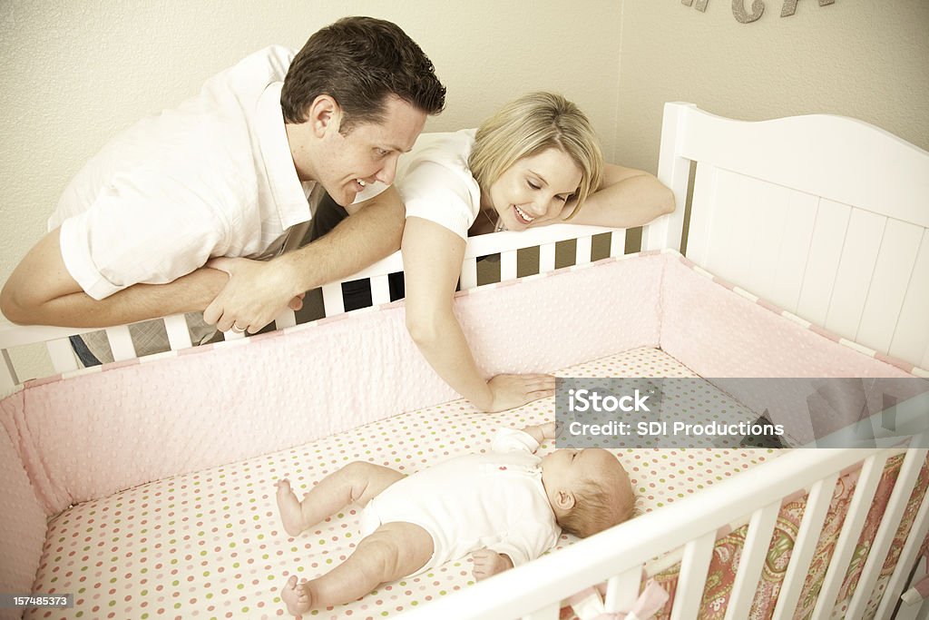 Felice giovane coppia caucasico adoring loro bambino nella sua culla - Foto stock royalty-free di Culla