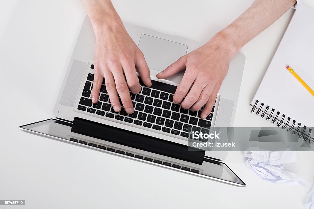 Searching For Inspiration Male hands typing on a laptop next to a notepad and crumpled sheets of paper, searching for ideas on a computer. Adult Stock Photo