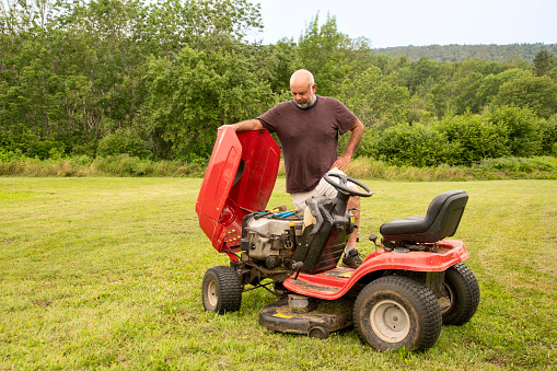 A man standing beside a broken down older lawn tractor in need of repair.