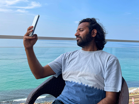 Stock photo showing close-up view of man taking selfie with phone camera with background view of railway train tracks of Coastal (southern) railway line in Colombo, Sri Lanka.