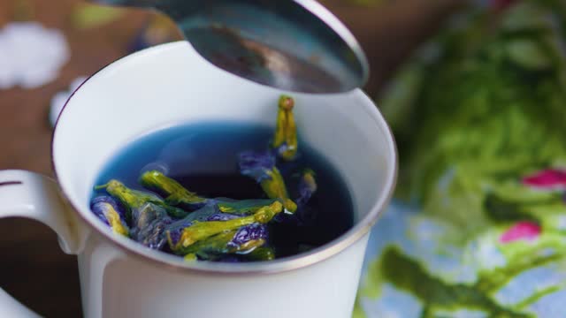 Pouring Blue Thai Anchan Butterfly pea flower tea into mug cup from teaspoon.