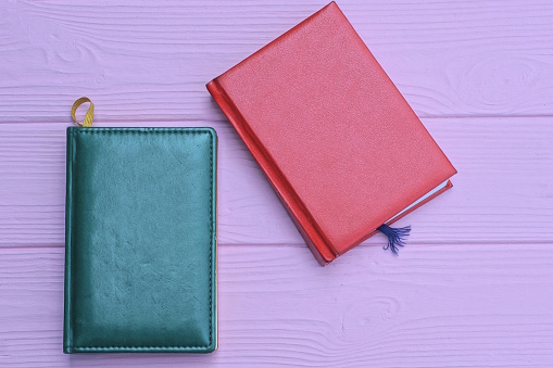 two closed red and green leather notebooks lie on a pink table