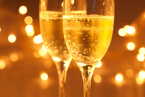 Two bubbly champagne flutes in a fairy light background. Selective focus.