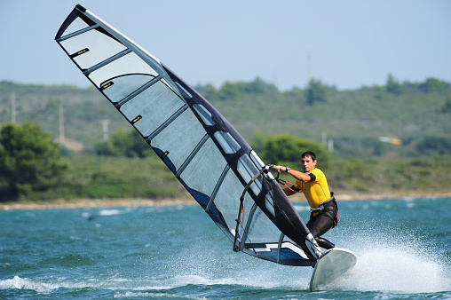 Young woman windsurfing on sea with board and colourful sail.