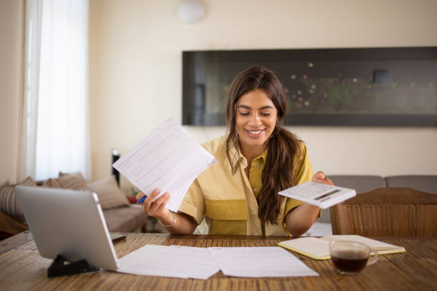 istock Young woman using calculator while going through bills and home finances 1575015730