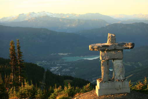 An inukshuk in Whistler, BC, Canada. This beautiful inukshuk - a rock statue that was symbolic for First Nations people - stands at the top of Whistler Mountain in the Whistler Blackcomb Resort in Whistler, British Columbia, Canada. The image was taken in summer. Coast Mountains in background. Nobody is in the image. 