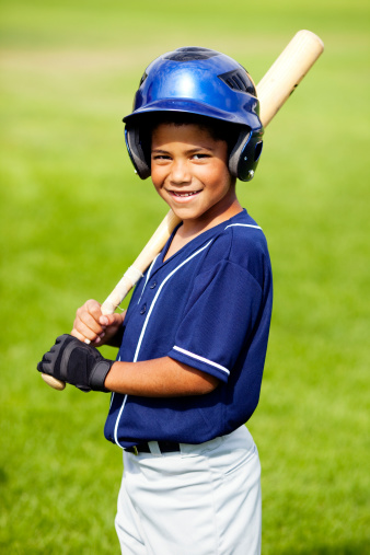 Adorable little boy is little league baseball player standing on local ballpark field