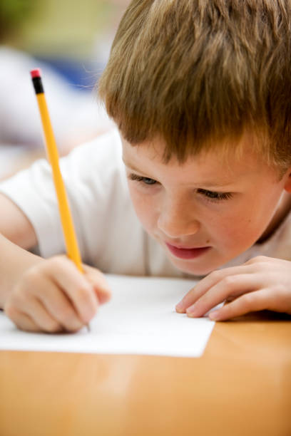 Closeup of little boy doing homework in the garden. The boy is 6 years old and is writing or drawing in the excercise book.