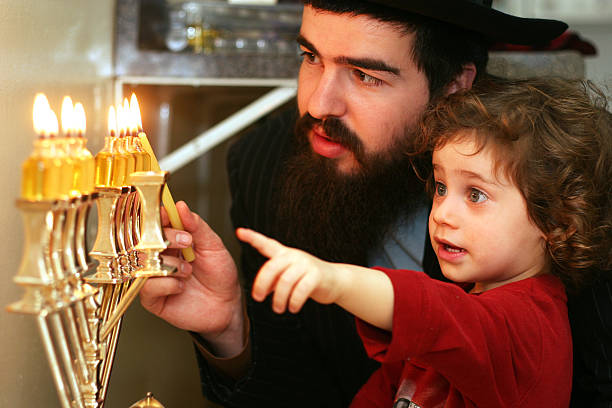 vater beim anzünden der menora - hanukkah menorah judaism religion stock-fotos und bilder