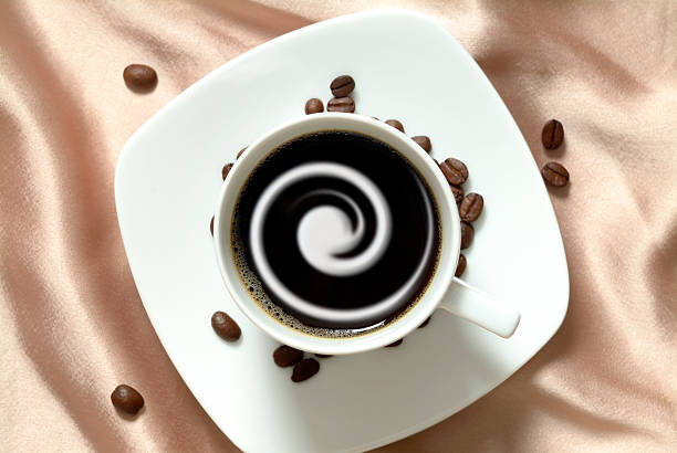 Black coffee with cream in china cup, brown satin background Black coffee with coffee cream in china cup arranged on satin background. Some coffee beans scattered around the cup on the background. black coffee swirl stock pictures, royalty-free photos & images