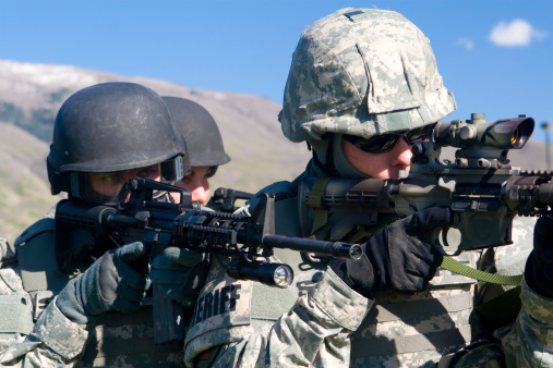 Three special forces team members in camouflage on patrol aiming rifles.