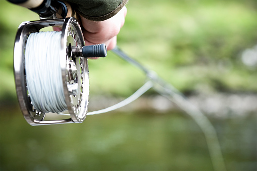 Close-up on a fishing reel as the rod is held out over the river.  Please note shallow depth of field.
