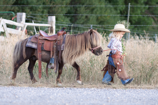 Little girl with cowboy hat, walking with her little horse.
