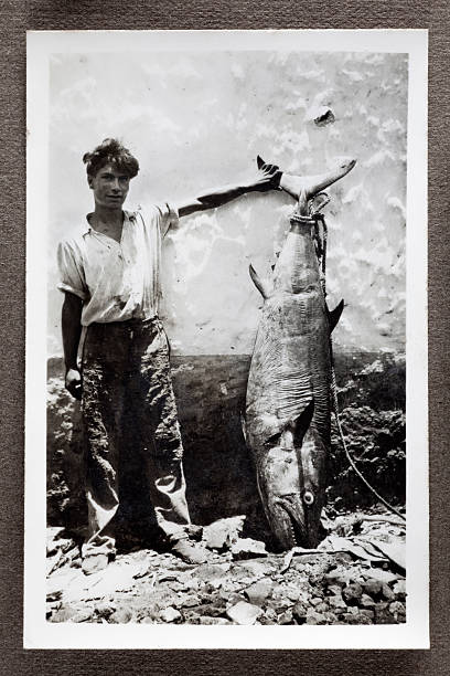 Fisherman With Bluefin Tuna Vintage black and white photograph of a peasant fisherman proudly showing off a large Bluefin Tuna leaning against a wall. Some dust and scratches which convey age of original image, taken in Mauritius, 1942. catch of fish photos stock pictures, royalty-free photos & images