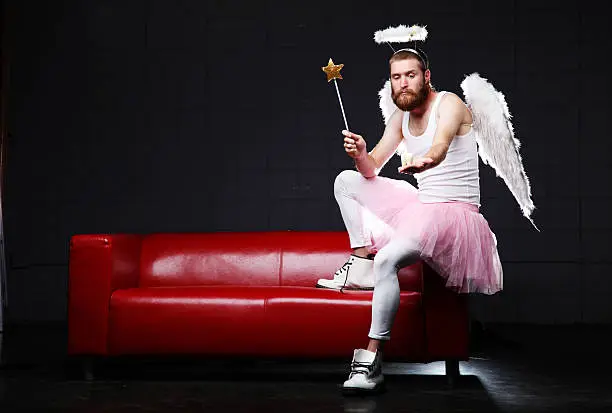 Humorous male  tooth fairy sitting on the arm of a couch with wand and giant molar.  Dark background and red couch.