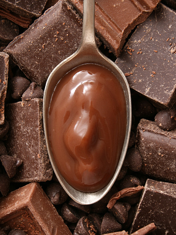 Top view of metallic spoon with chocolate pudding on it and chocolate pieces beneath it