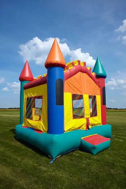 Stock photo of a children's bouncy castle inflatable jumper playground in a grass field with a blue sky.