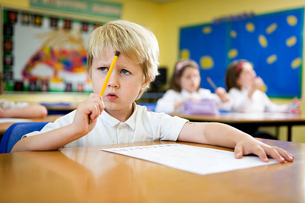 primary school: young boy concentrating over a challenging maths problem stock photo