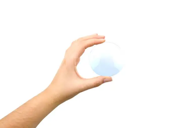 Photo of Hand holding an eyeglass lens without the glasses on white