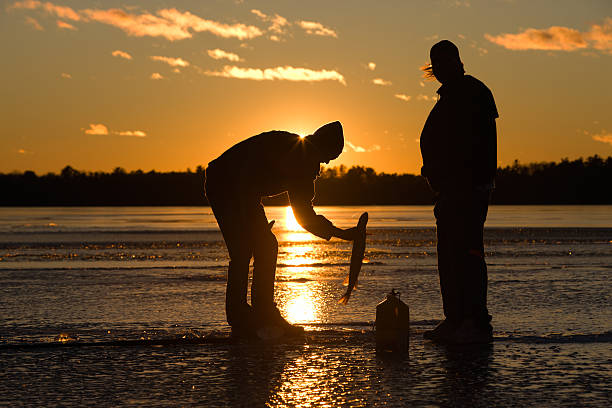 Ice fisherman catching fish on frozen lake at sunset. stock photo