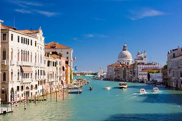 The Grand Canal and Santa Maria della Salute church in Venice, Italy. Boats moving on the river under a clear blue summer sky.