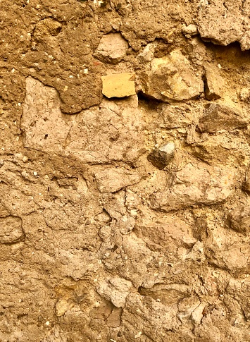 Vertical closeup photo of a variety of ochre coloured local stones mortared together and rendered with clay in a house wall in the old centre of the historic town of Aix-en-Provence, south of France.