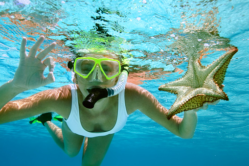 woman snorkeling with a starfish, showing the O.K. signal underwater