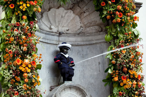 Mannekin Pis in Brussels Belgium with a full stream spraying forth as he wears a military uniform