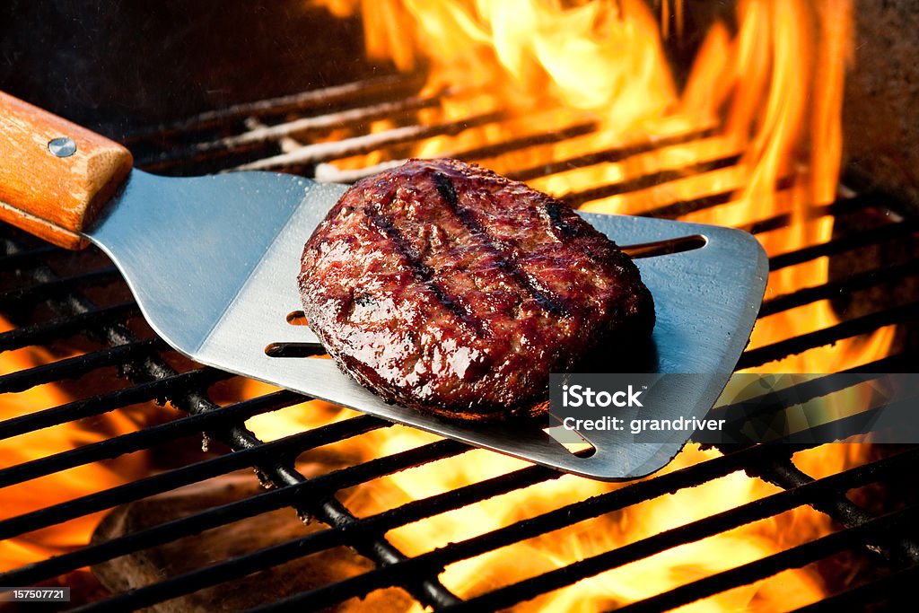 Hamburger Patty on Grill with Fire Juicy burger with appetizing grill marks on a silver spatula over a flaming charcoal barbecue grill Barbecue Grill Stock Photo