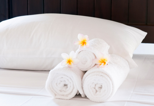 Wellness and spa concept background with a bed decorated white lily flowers and rolled towels. Rolled towels on massage table in empty spa salon or room. Interior of aesthetic clinic