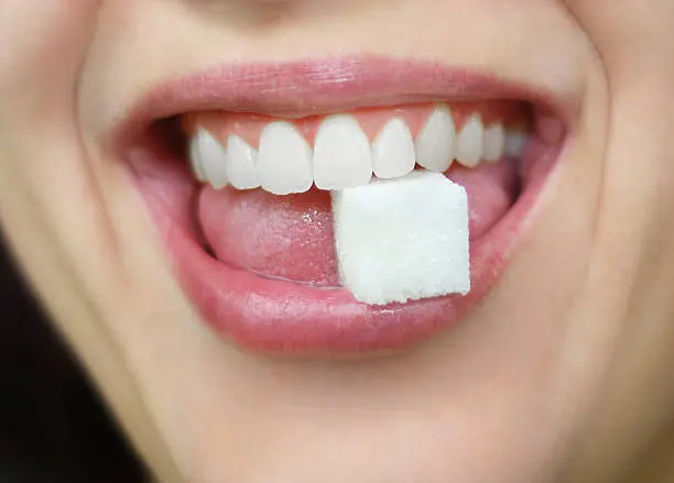 Close up of a woman holding a sugar cube between her teeth in her mouth.  