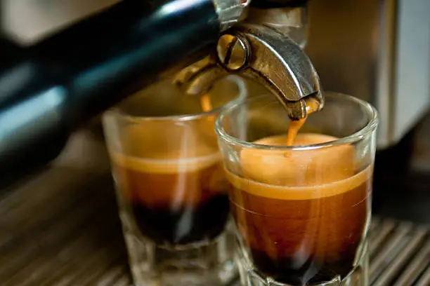 Dual espressos being made from a commercial grade machine in a local coffee shop.  Shots are being made into glass shot glasses.  Crema on the top shows that this is high quality coffee.
