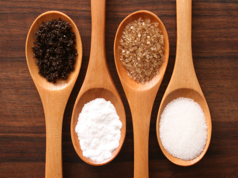 Four spoons with varieties of sugar (black,powder,brown,white)