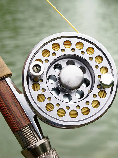  Fly fishing reel and part of rod with water background.