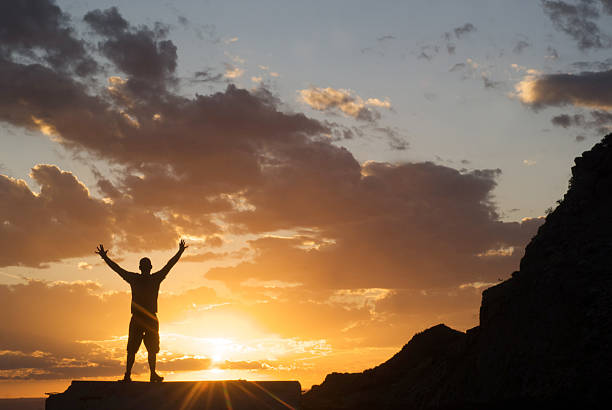 istock silhouette man arms raised into sunset sky 157509768