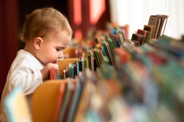 Little girl in library Little girl flicking trough books in a library. Natural light. babies only stock pictures, royalty-free photos & images