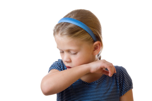 Cute little blond girl coughing in her elbow isolated on white- the technique  recommended by the U.S. Centers for Disease Control and Prevention and the American Academy of Pediatrics.  