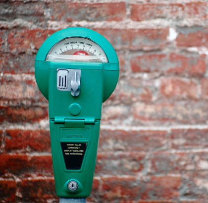 Green parking meter with old brick wall in the background out of focus.All manufacture ID has been removed