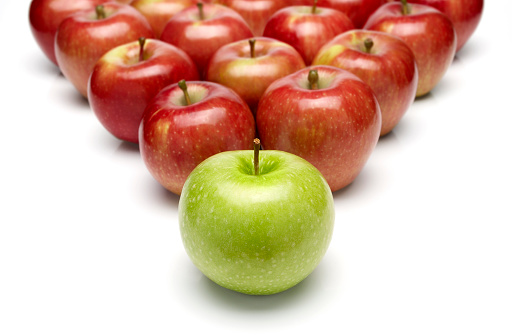 A green apple as a leader at first and lots of red apples as a crowd at background 