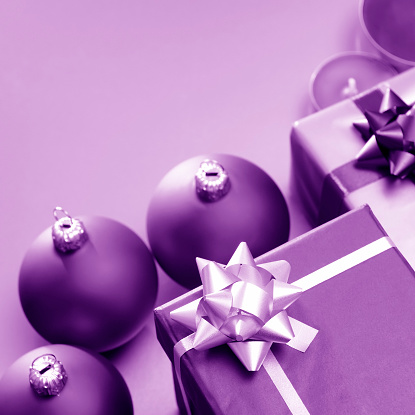 Two beautiful purple gift boxes with ribbons, some baubles and candles on a lilac background. Copy space, studio shot.